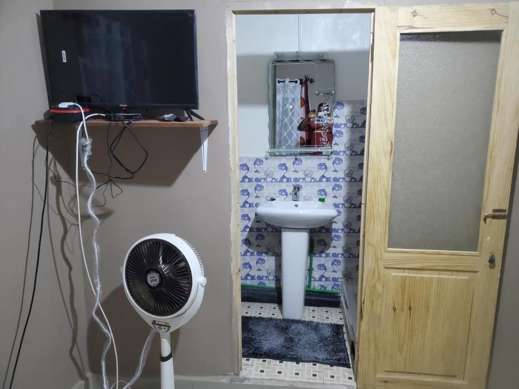 Un bany amb televisió sobre una estant, un ventilador, un lavabo i una porta.