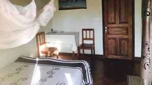 A room with a bed, a wooden door, a table with chairs, and a painting on the wall.