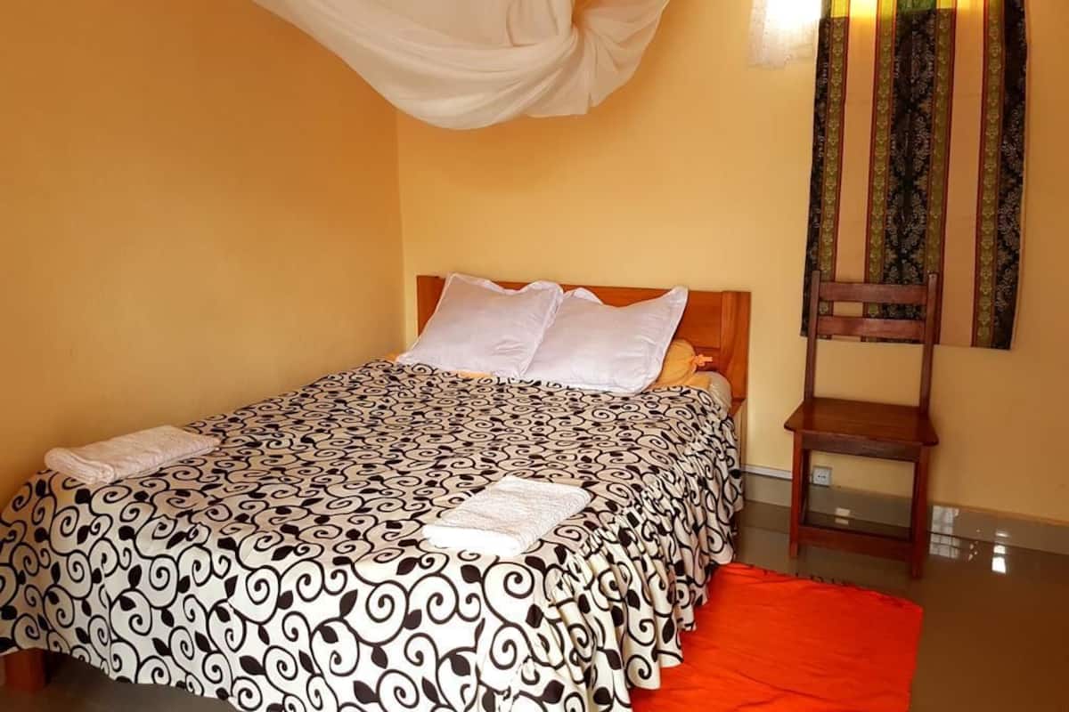 Una cama con colcha estampada, cabecera de madera y dosel blanco.