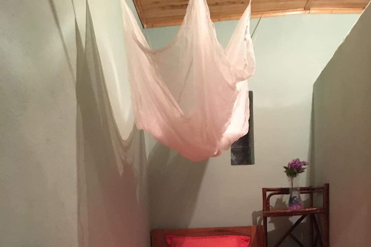 Un dormitorio pequeño con una cama individual, una silla, un sillón de madera y un dosel colgante.