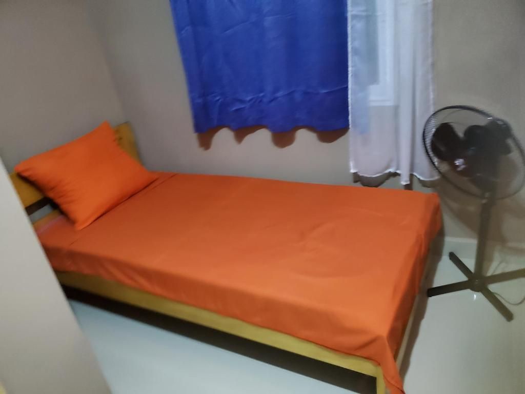 Una stanza piccola con un letto singolo, una ventola portatile e una tenda.