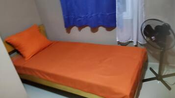 Una stanza piccola con un letto singolo, una ventola portatile e una tenda.