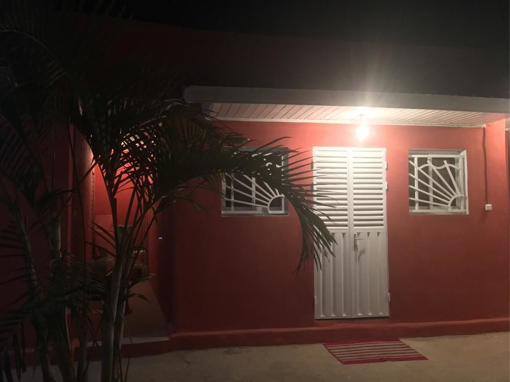 Un edificio rojo con contraventanas y puerta blancos, rodeado de palmeras.