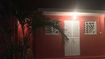 Un edificio rojo con contraventanas y puerta blancos, rodeado de palmeras.