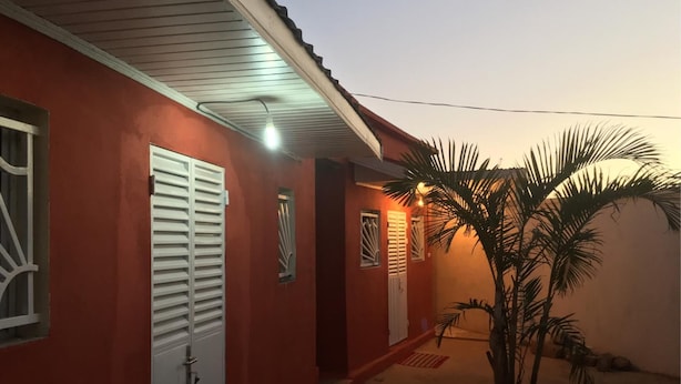 A red building with white doors and windows, a palm tree, and a tiled floor.