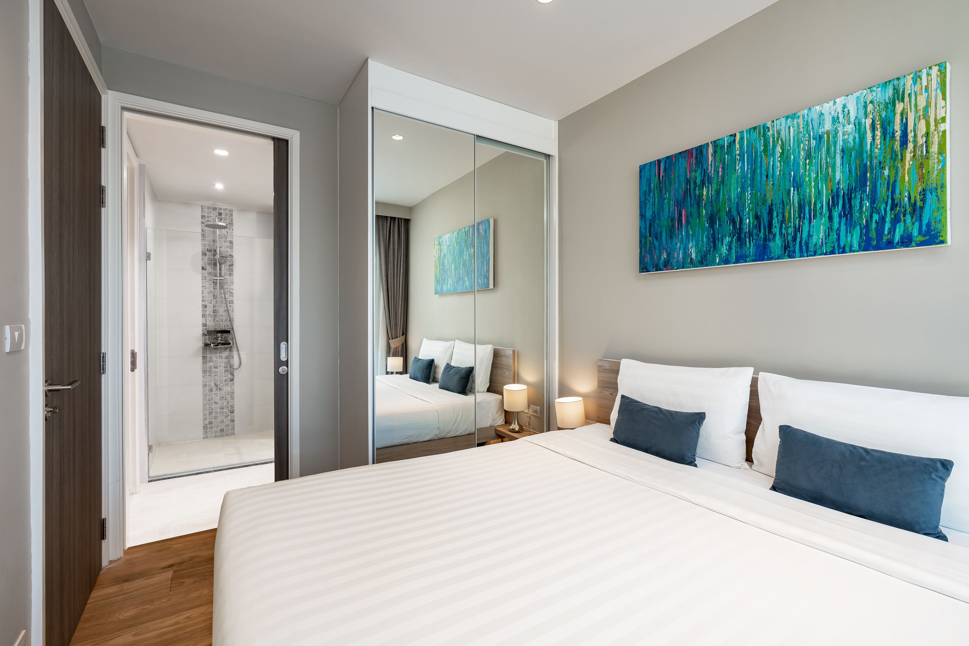 A modern hotel room with a large bed, a walk-in closet, a shower area, and a large abstract painting on the wall.
