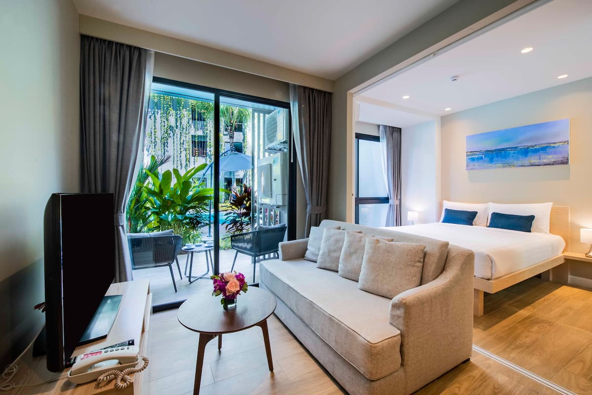 Quarto de hotel moderno com sofá, cama, mesa pequena com um vaso de flores, telefone e vista do exterior por grandes janelas.