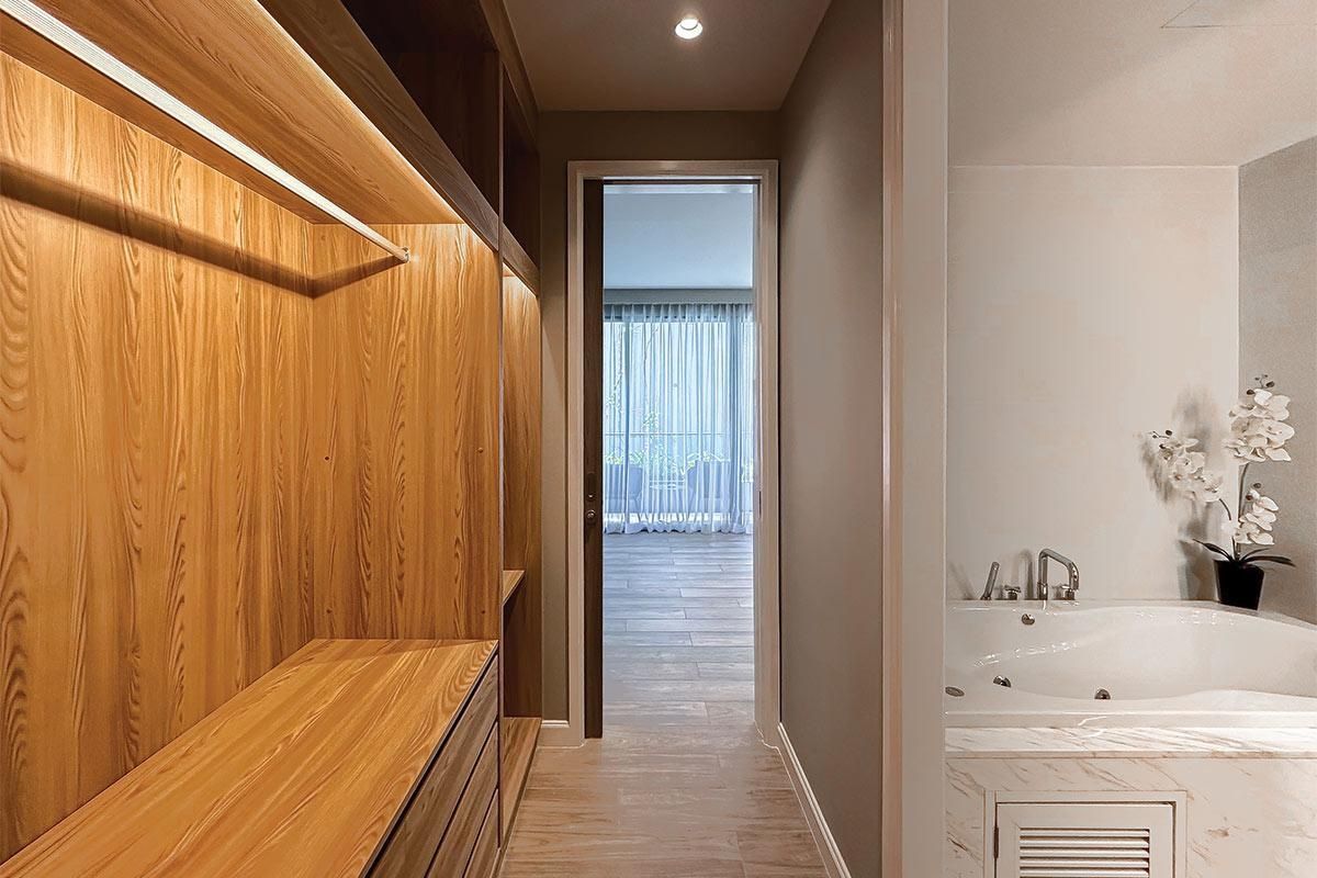 A modern bathroom with a wooden bench, a bathtub, and a view of a balcony.