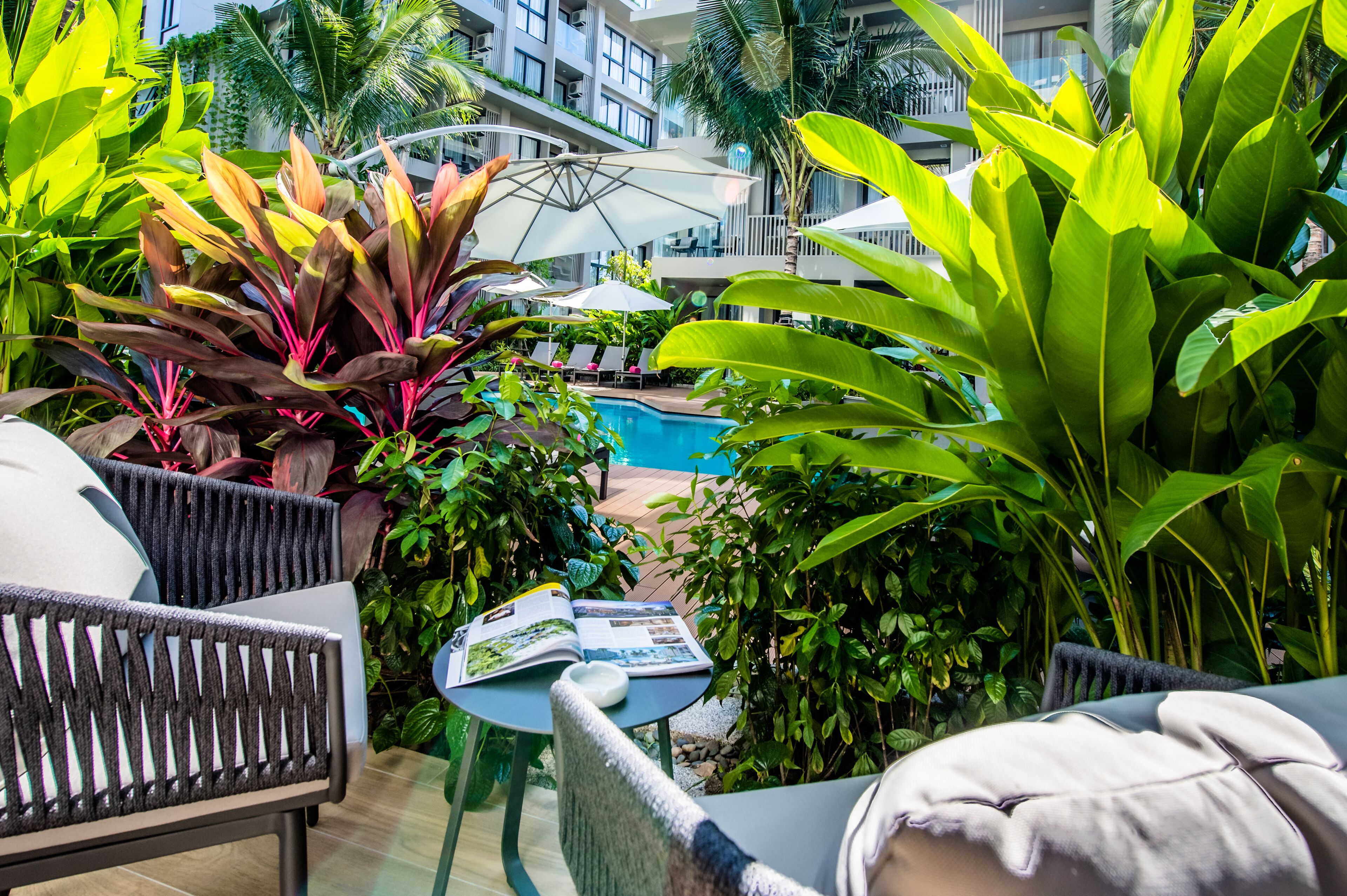 A poolside area with lounge chairs, umbrellas, and lush greenery.