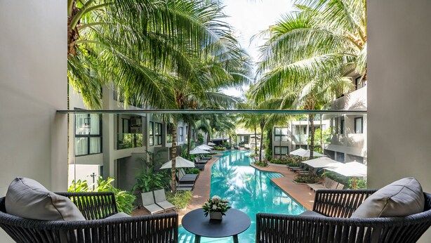 A balcony with wicker chairs and a small table, overlooking a swimming pool surrounded by palm trees and lounge chairs. - Diamond Resort Phuket Official Account (Choeng Thale)
