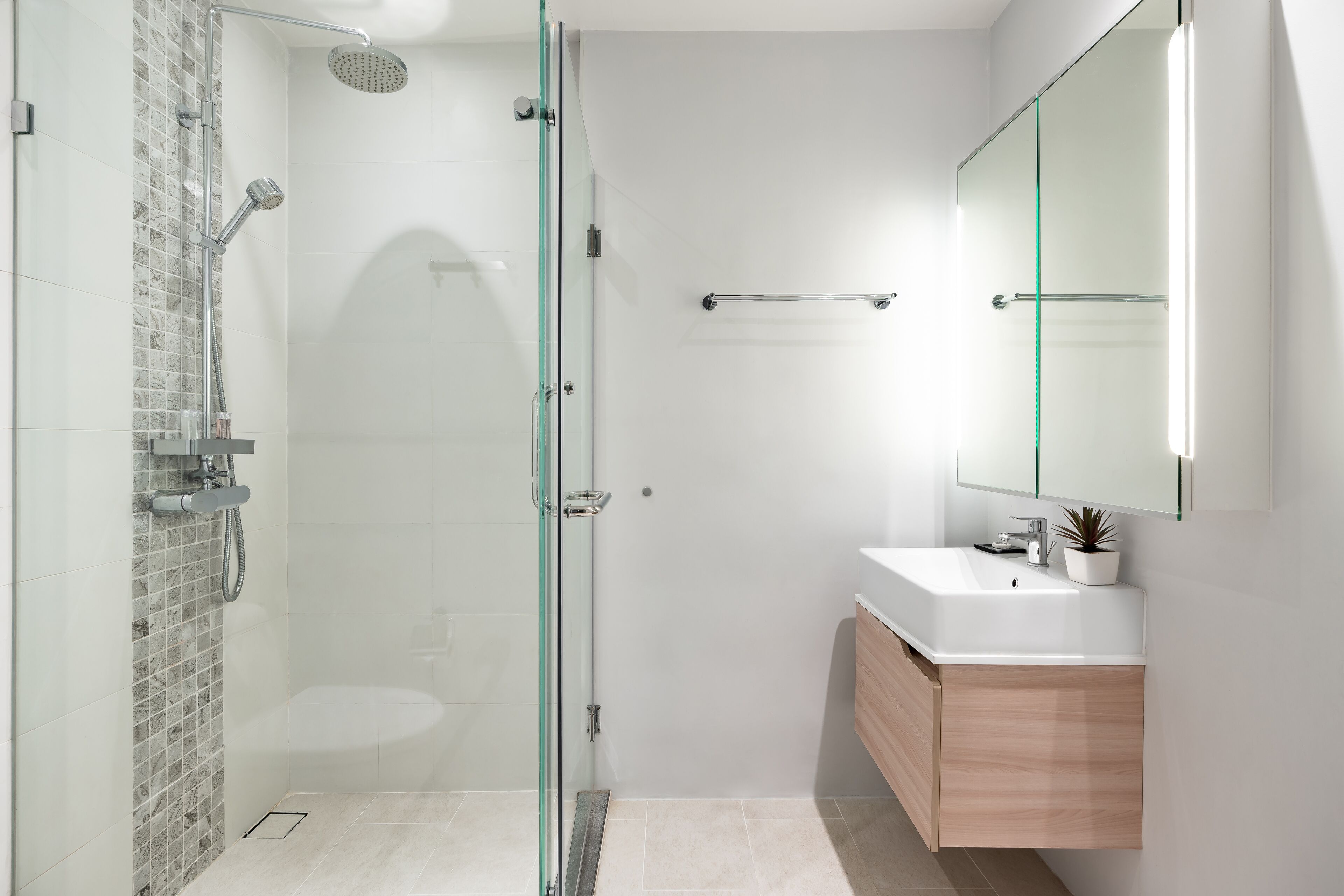 A modern bathroom with a glass shower enclosure, a white sink, and a wooden vanity.