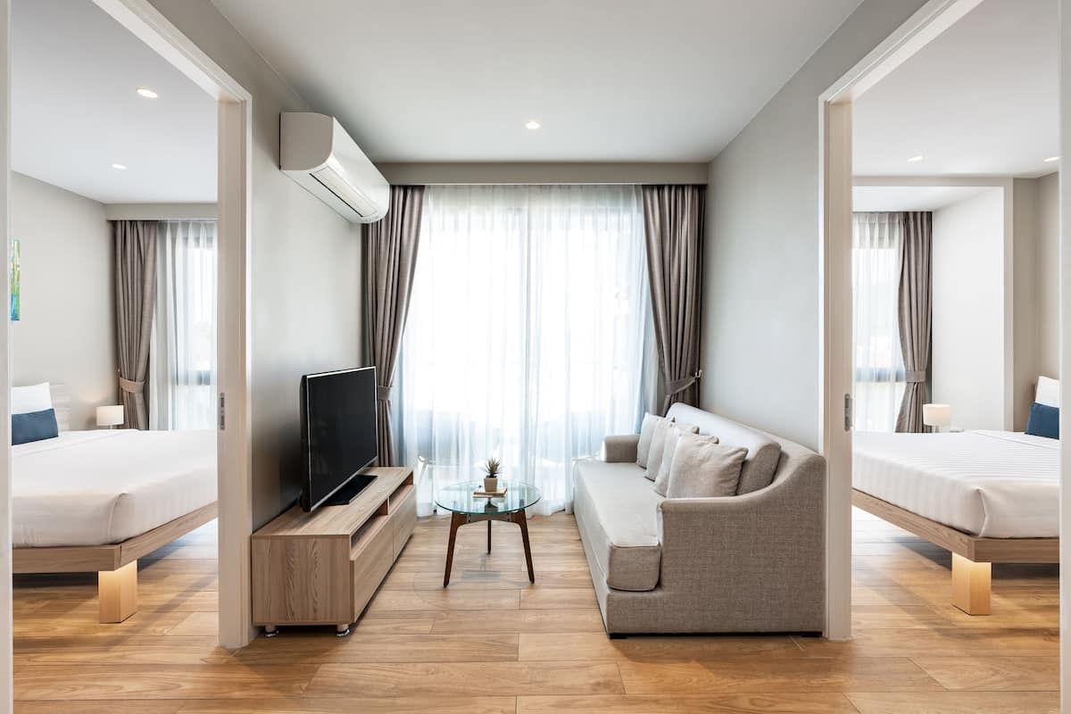 Quarto de hotel moderno com sofá, duas camas, TV e mesa de centro de vidro.