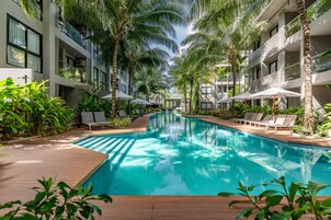 Un área de piscina con sillones reclinables y sombrillas, rodeada de palmeras y follaje.