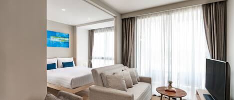 A modern hotel room with a sofa, a TV, a small table, and a bed with a large window.