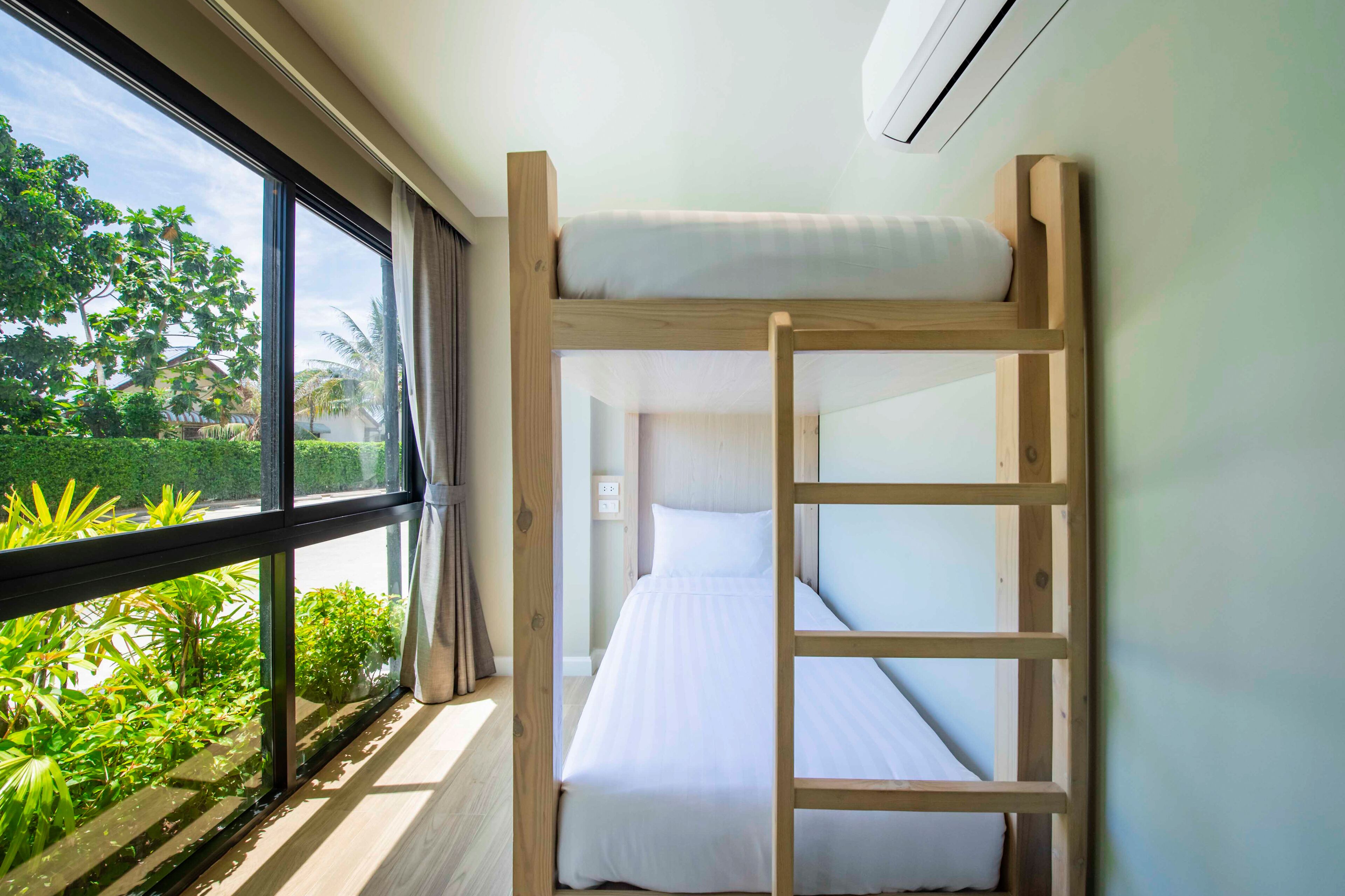 Una cama litera con escalera, una ventana con cortinas y vistas a vegetación.