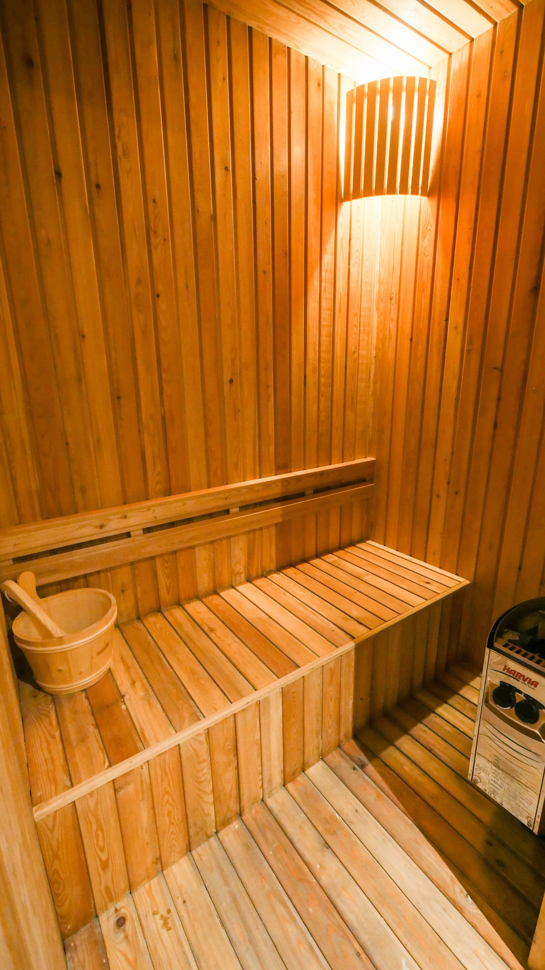 A wooden sauna with a bench, a wooden bucket, and a sauna box.