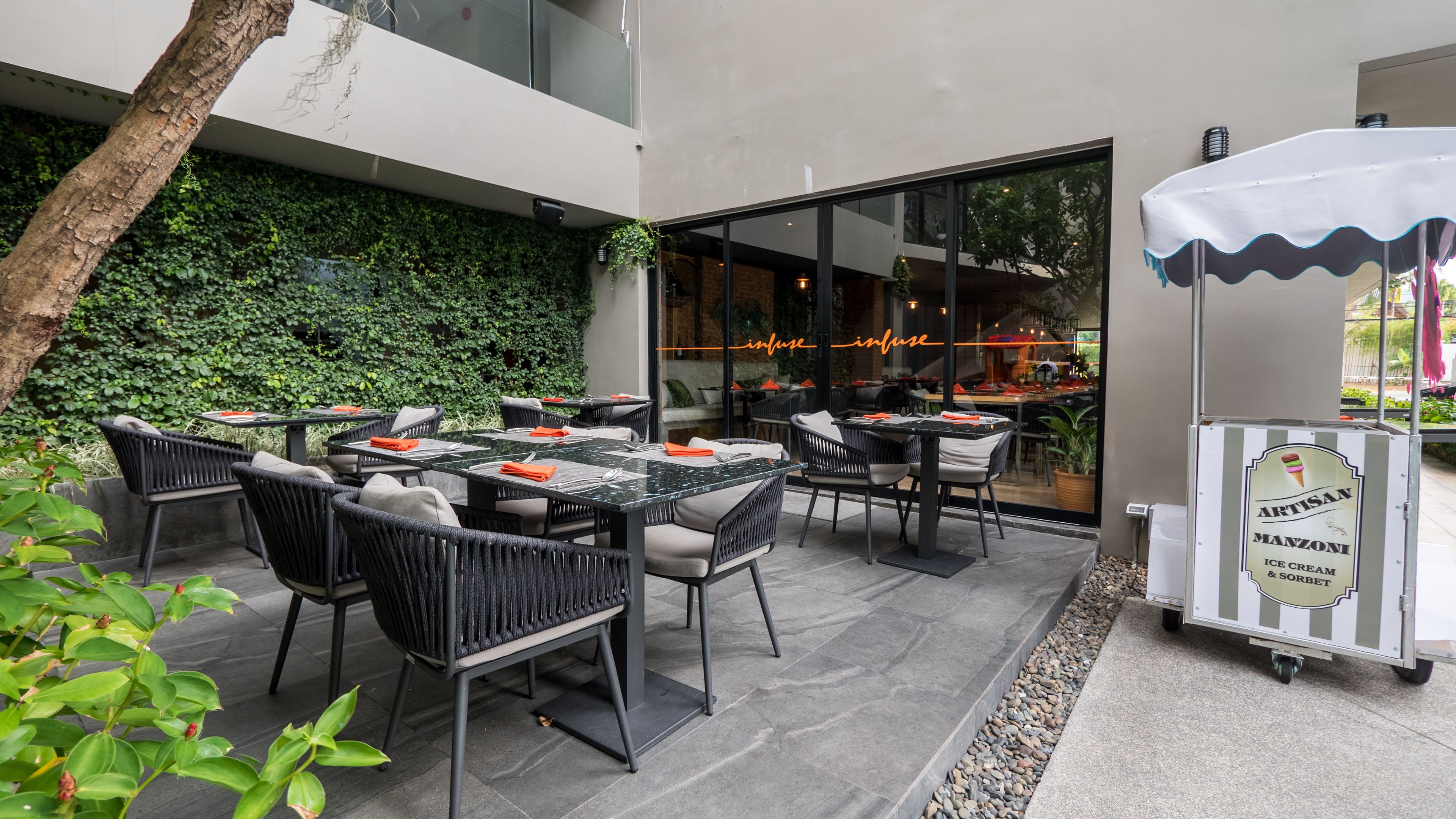 Un espacio exterior para comer con mesas y sillas, un muro de vidrio y un letrero para helados y sorbetes Artisan Manzoni.