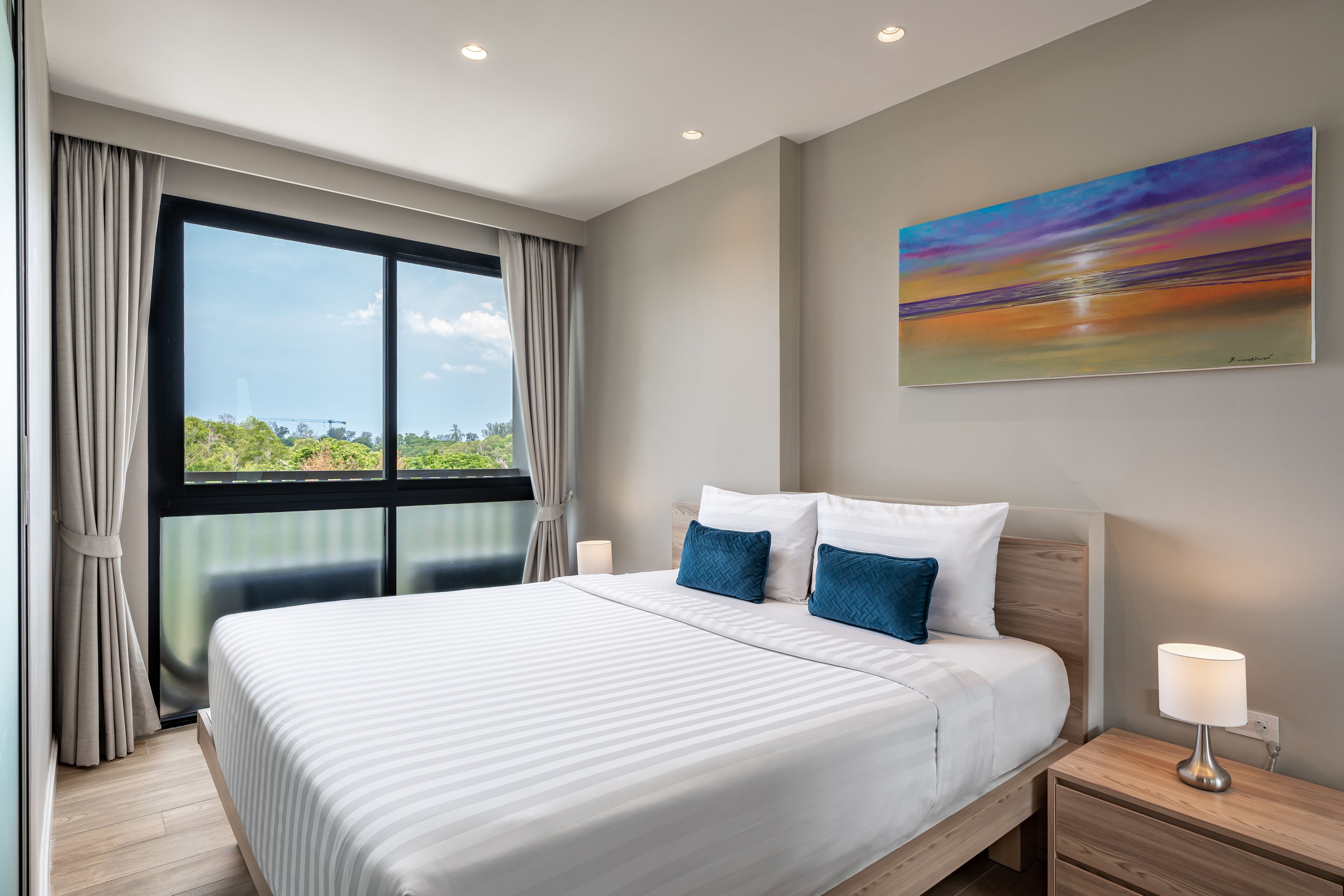 A modern hotel room with a large bed, a nightstand, a lamp, and a painting on the wall.