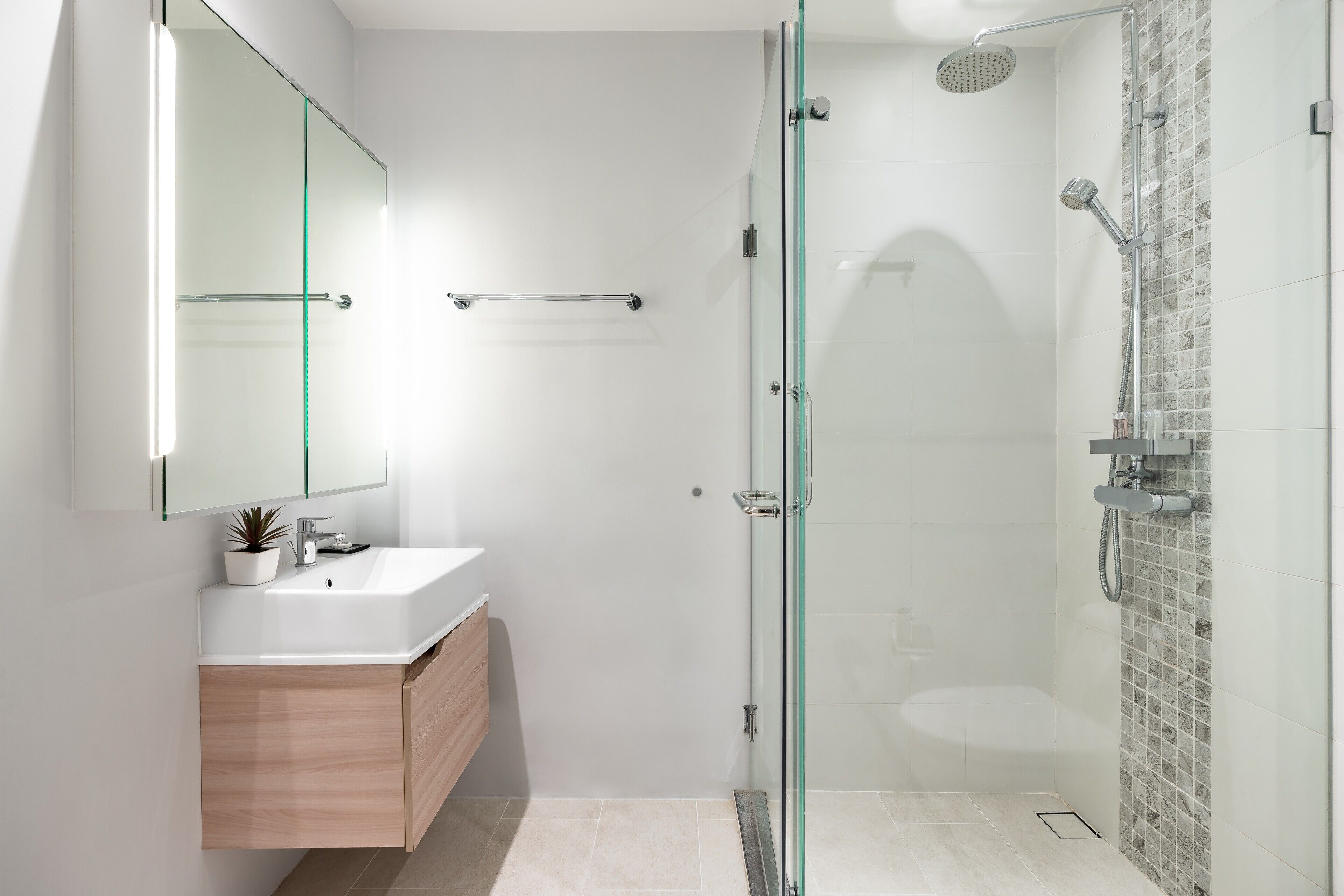 Une salle de bain moderne avec une douche à l’italienne en verre, un lavabo blanc et un meuble-lavabo en bois.