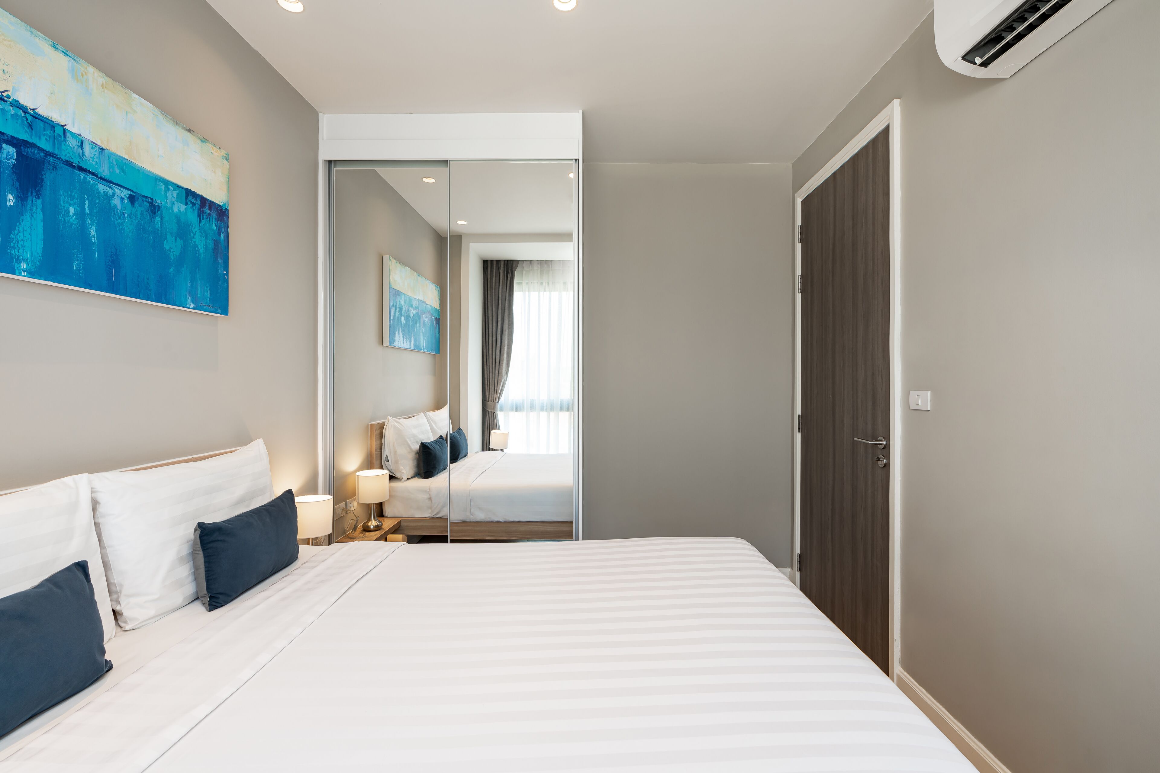 A modern hotel room with a large bed, bedside tables, a mirror, and artwork on the walls.