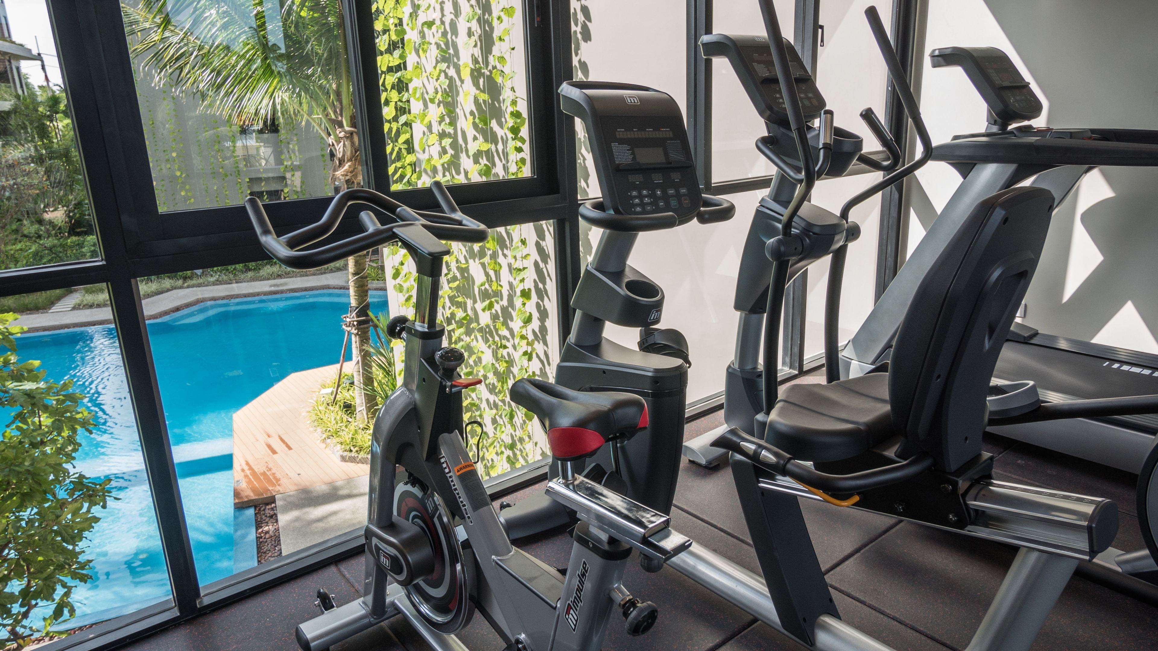Un gimnasio con equipo de ejercicio, piscina y vistas a zonas verdes.