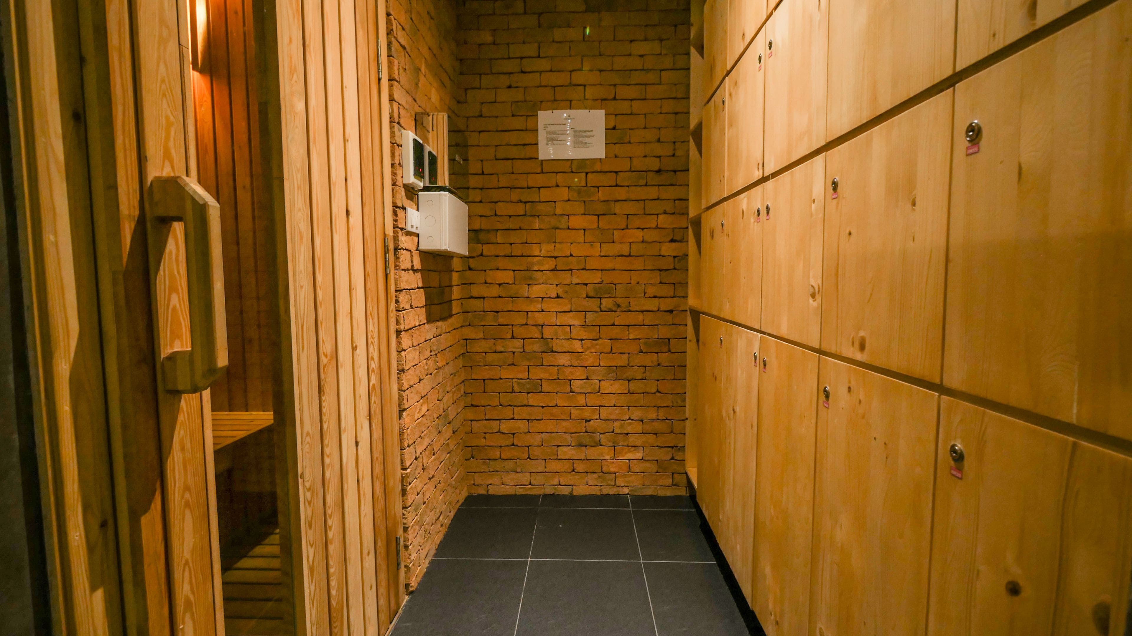 A narrow hallway with wooden lockers on one side and a brick wall on the other.