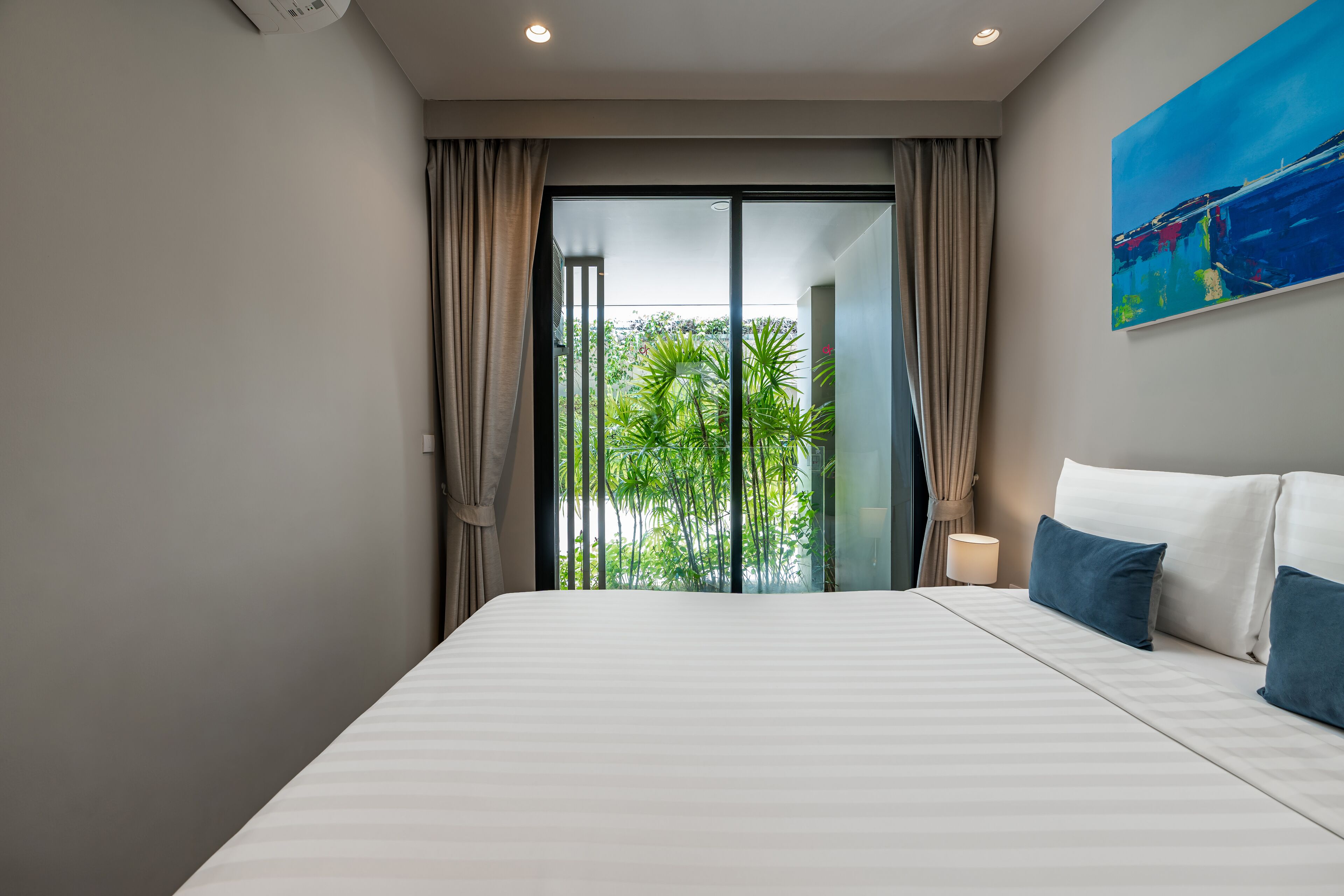 Una habitación de hotel moderna con una cama grande, vistas a la vegetación a través de una puerta corredera y un cuadro en la pared.