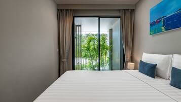 Una habitación de hotel moderna con una cama grande, vistas a la vegetación a través de una puerta corredera y un cuadro en la pared.