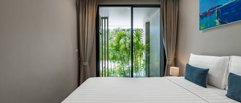 Una habitación de hotel moderna con una cama grande, vistas a la vegetación a través de una puerta corredera y un cuadro en la pared.