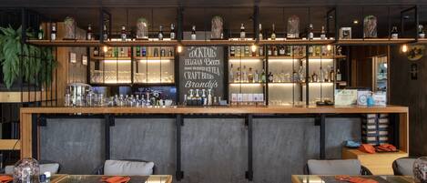 A bar area with shelves of bottles and glasses, a chalkboard menu, and seating with tables and chairs.
