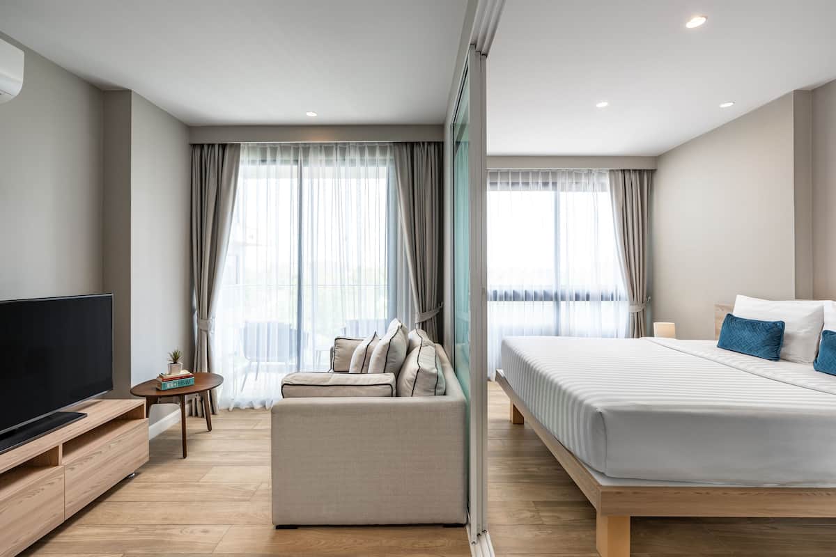 Quarto de hotel moderno com uma cama grande, um sofá, uma TV e uma pequena mesa com uma planta.