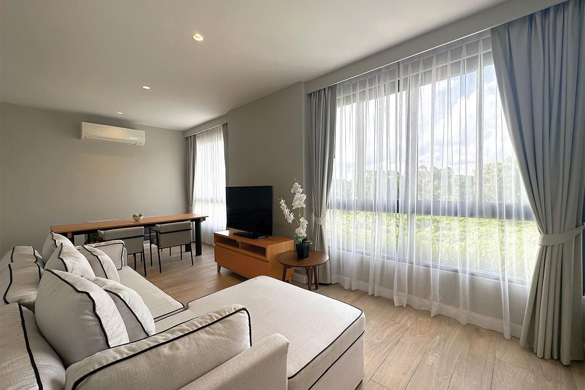 A modern living room with a sofa, a TV, a dining table, and a balcony with curtains.
