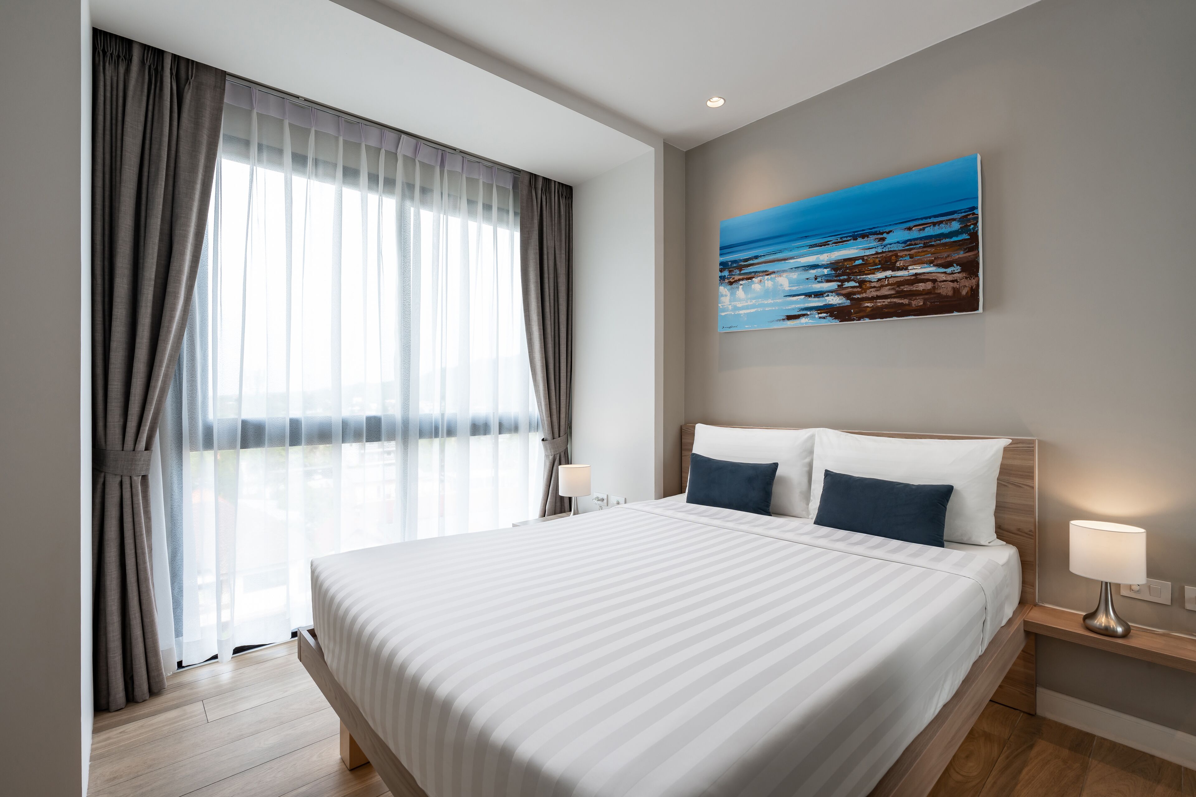 Una habitación de hotel con una cama grande, una mesita de noche, una lámpara de pared y un cuadro con una escena de playa.