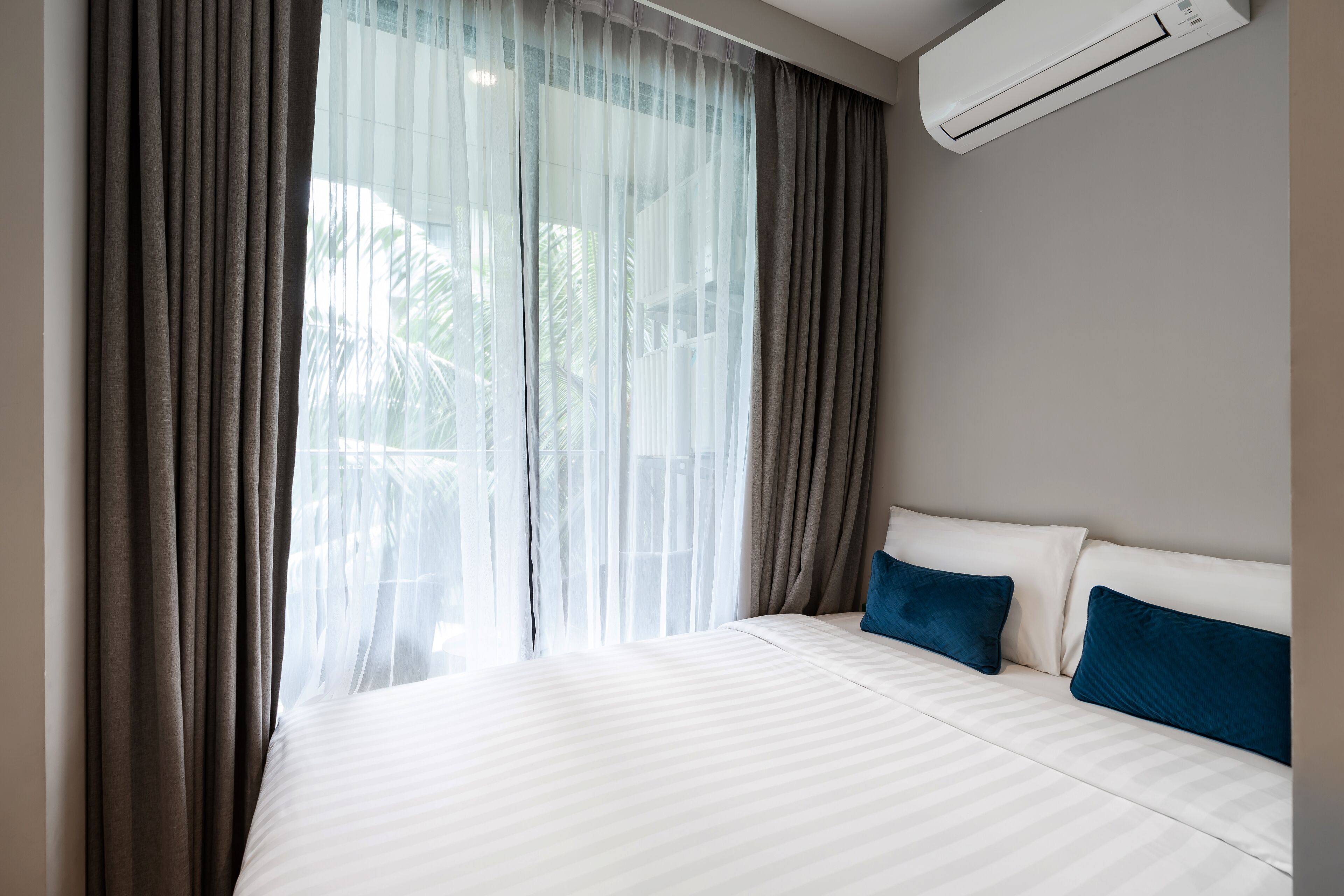 Hotelkamer met een groot bed, twee kussens, een raam met dunne gordijnen en een airconditioning.