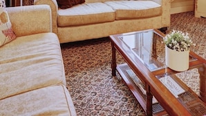 Ein Wohnzimmer mit einem beigefarbenen Sofa, einem passenden Sessel und einem Couchtisch aus Holz mit einem Blumentopf.