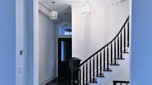 A hallway with a wooden staircase, a door leading to another room, and a light fixture above the staircase.