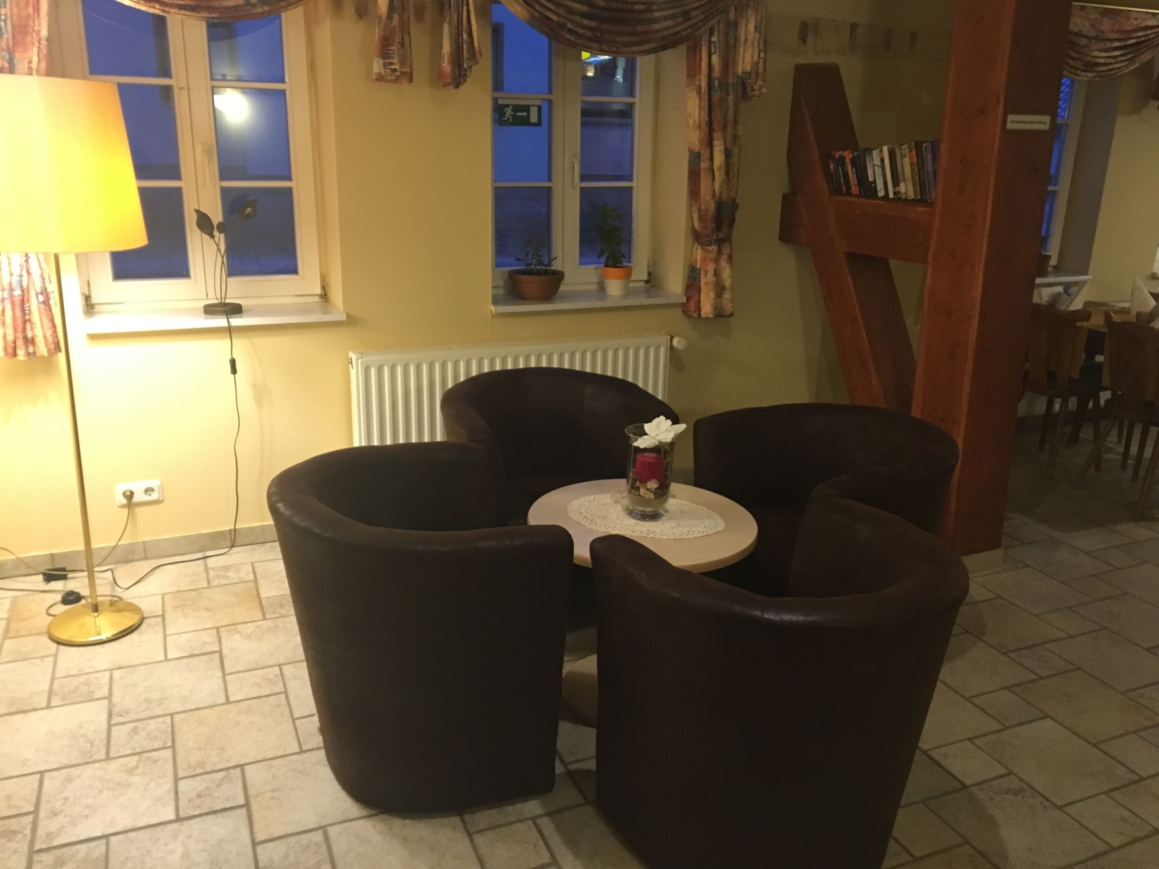 A cozy room with a round table, two armchairs, a lamp, a radiator, and a bookshelf.