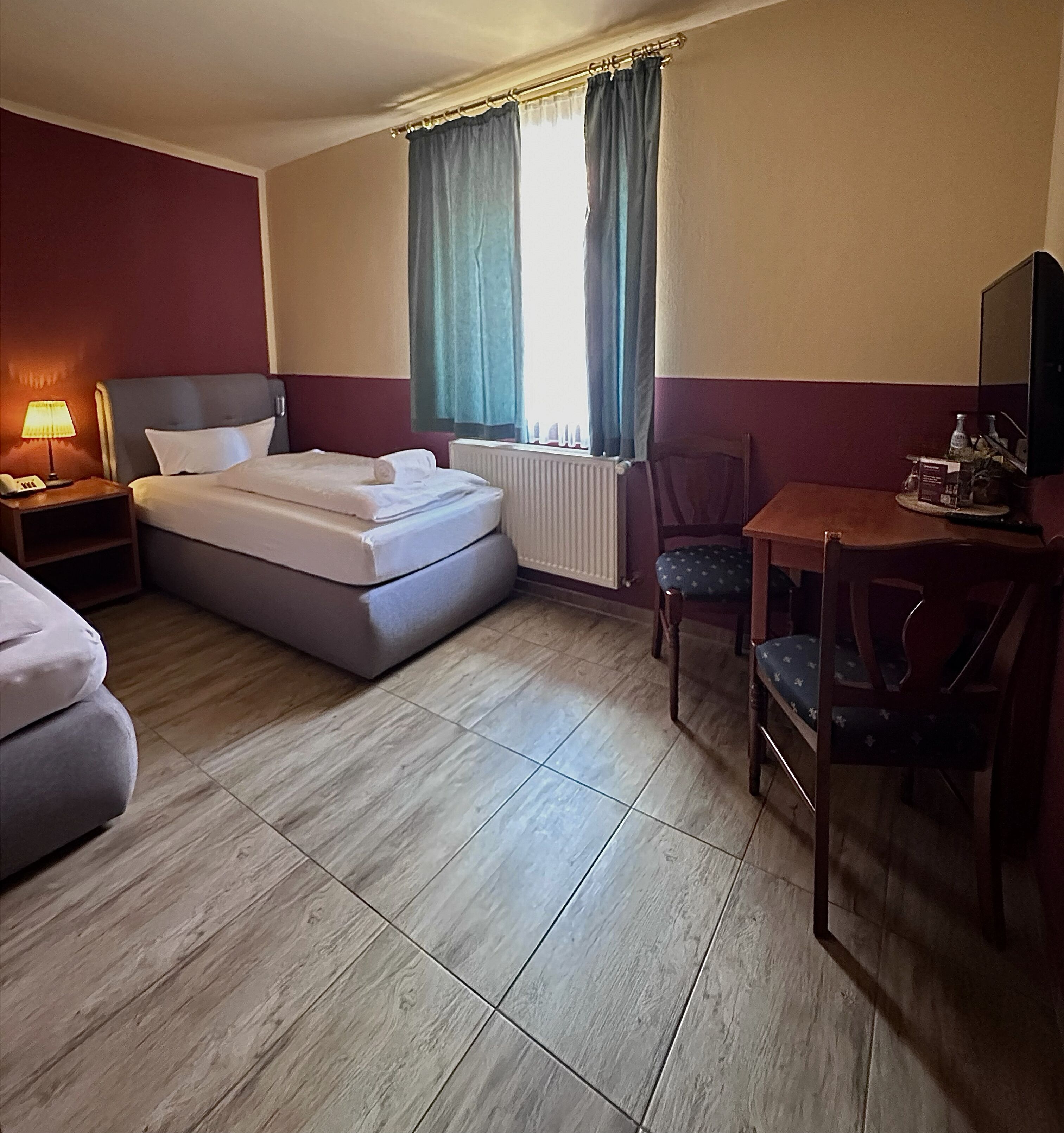 A hotel room with a bed, a desk, a chair, a lamp, and a window with curtains.