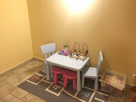 A small children's play area with a white table, two chairs, a red stool, and a toy.