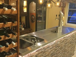 Angolo bar con lavello in acciaio inossidabile, bottiglie di vino su un portabottiglie e una parete in pietra.