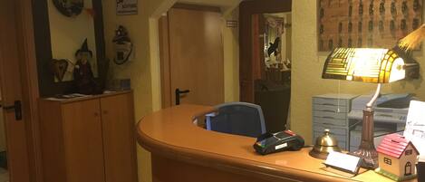 A reception desk with a computer, a lamp, and a small house model. There is a sign indicating a lobby and a door to a room.