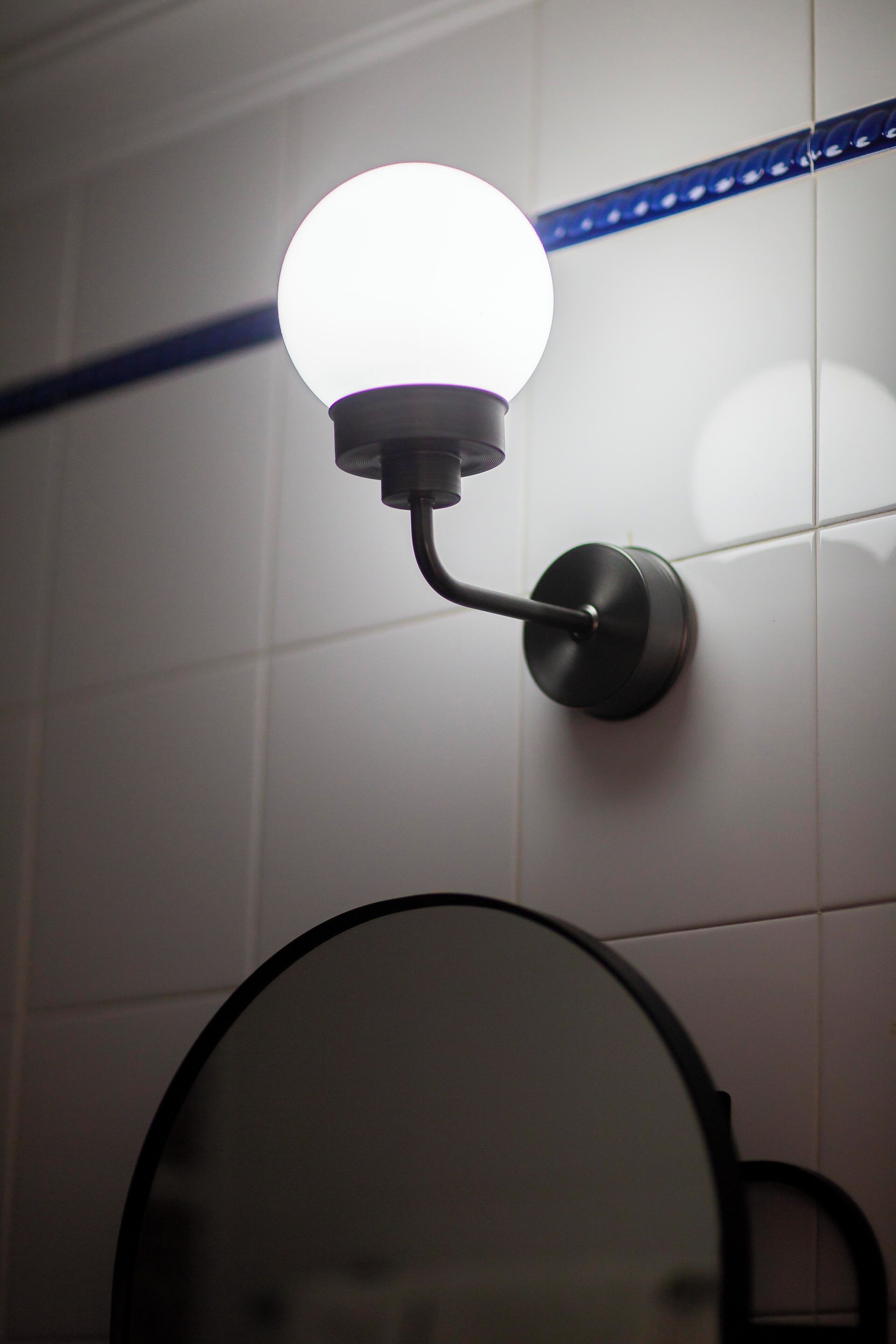 A bathroom with a round mirror, a wall-mounted light fixture, and a blue decorative strip.