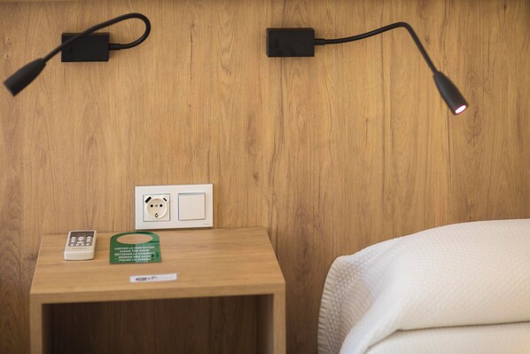 A wooden nightstand with a power strip, a thermostat, and a remote control. - Pensión dulces sueños (Seville)