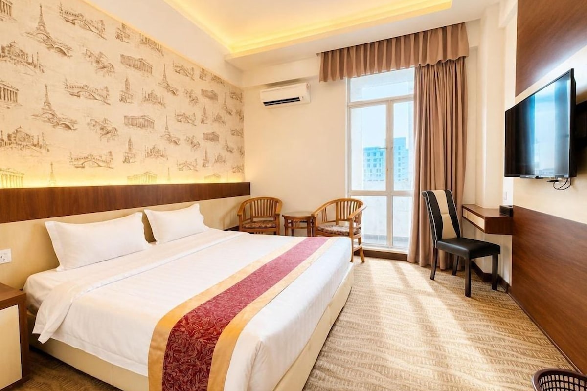 Une chambre d’hôtel avec un grand lit, un bureau, une chaise, une télévision et une fenêtre avec des rideaux.