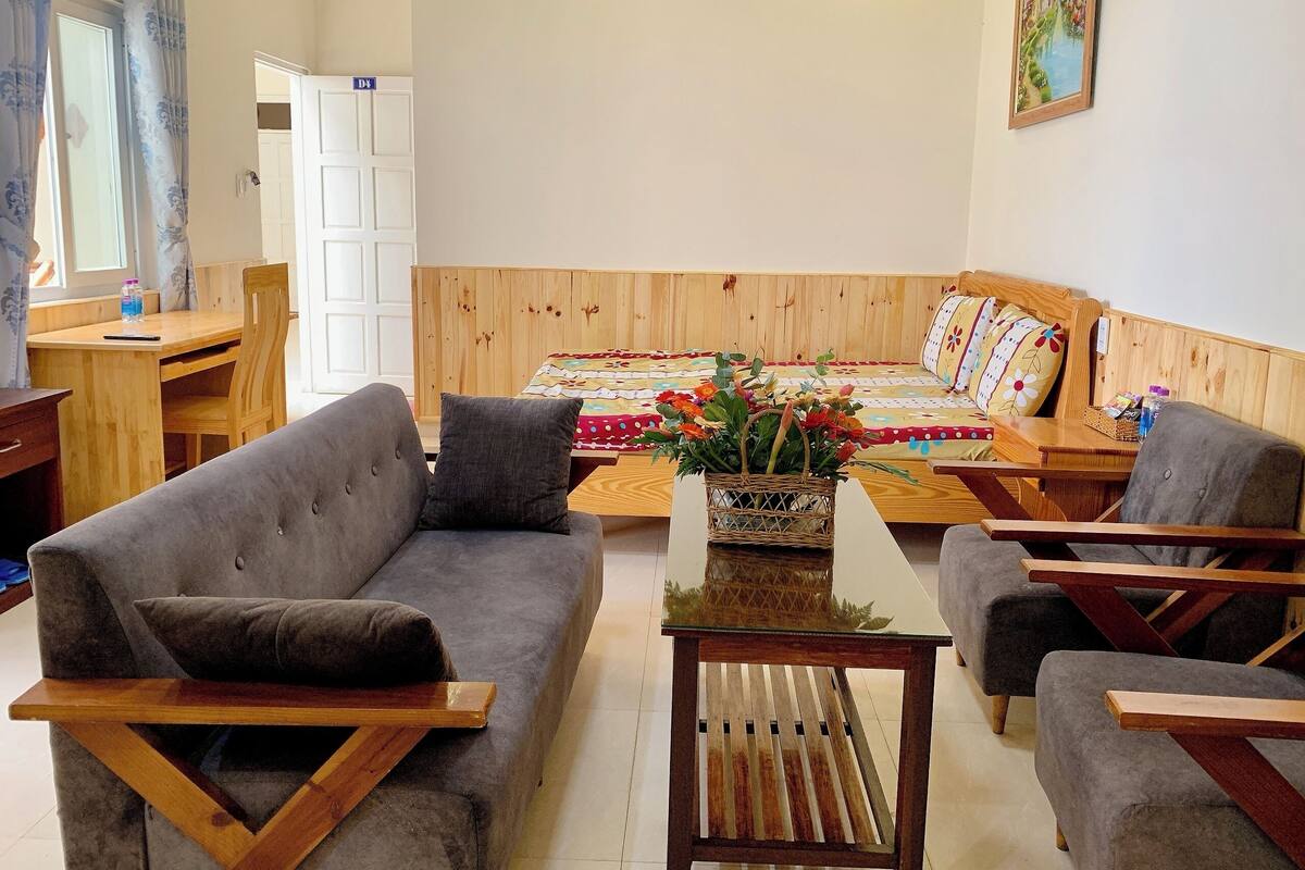 A cozy living room with a sofa, armchairs, a wooden coffee table, and a bed with a colorful quilt.