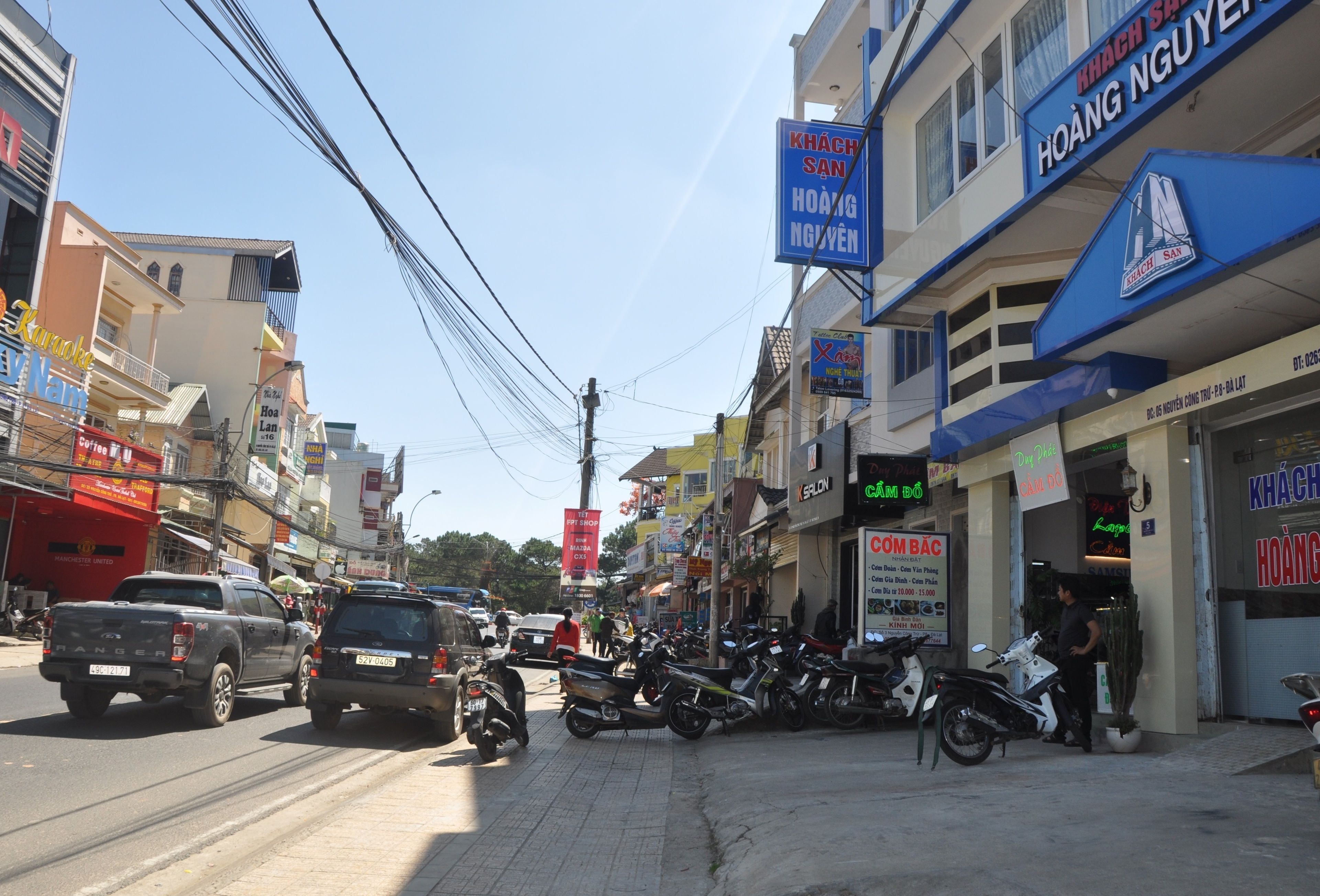 A busy street with various shops and motorcycles parked along the sidewalk.