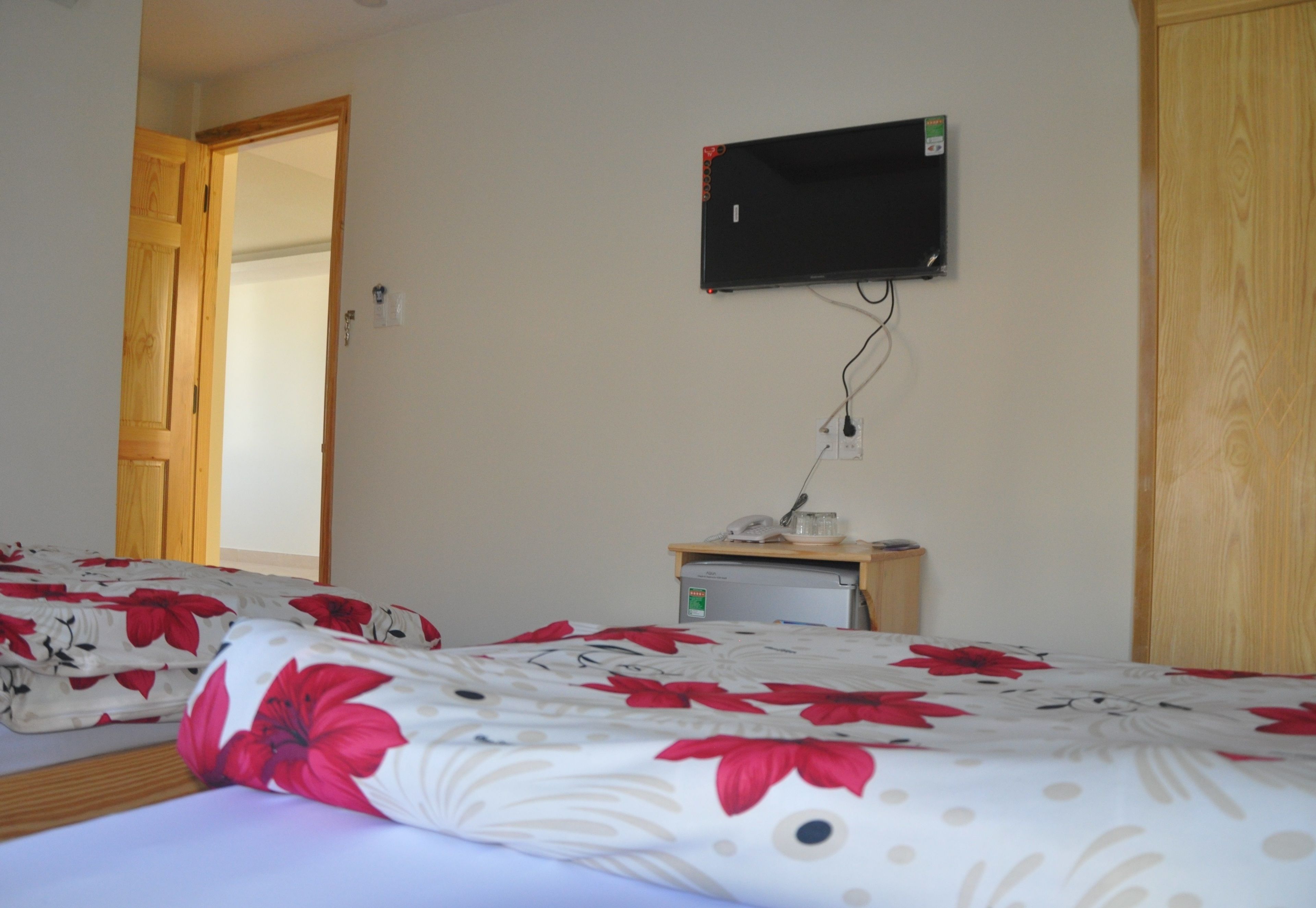 Une chambre à coucher avec un lit, un téléviseur fixé au mur et un petit bureau équipé d’un réfrigérateur.