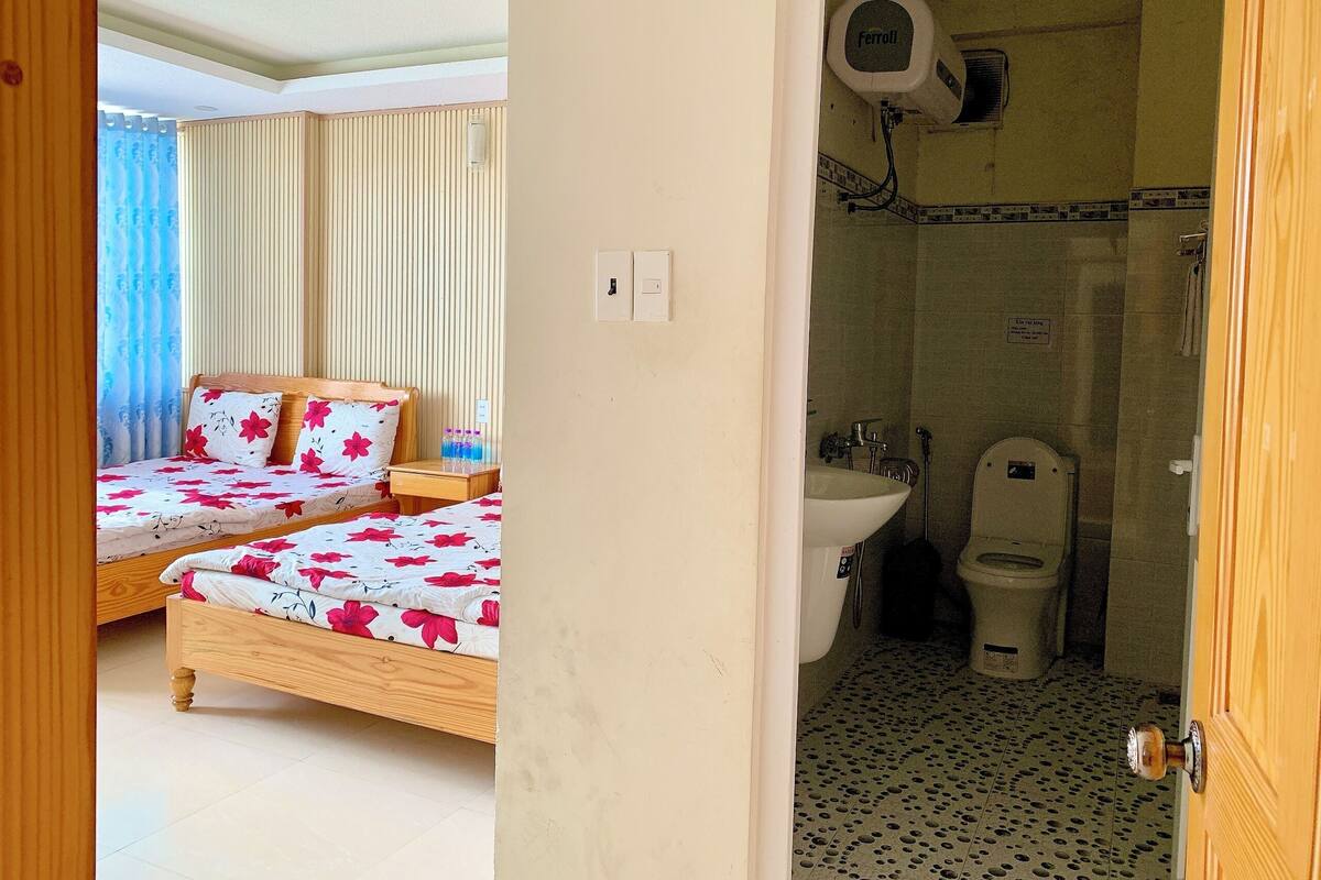 A hotel room with two beds, a bathroom with a sink and toilet, and a shower.