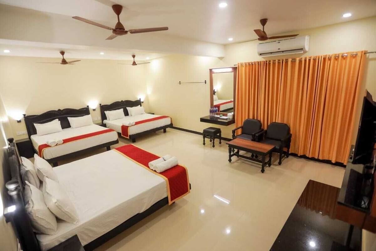 A hotel room with three beds, a desk, two chairs, a television, and ceiling fans.