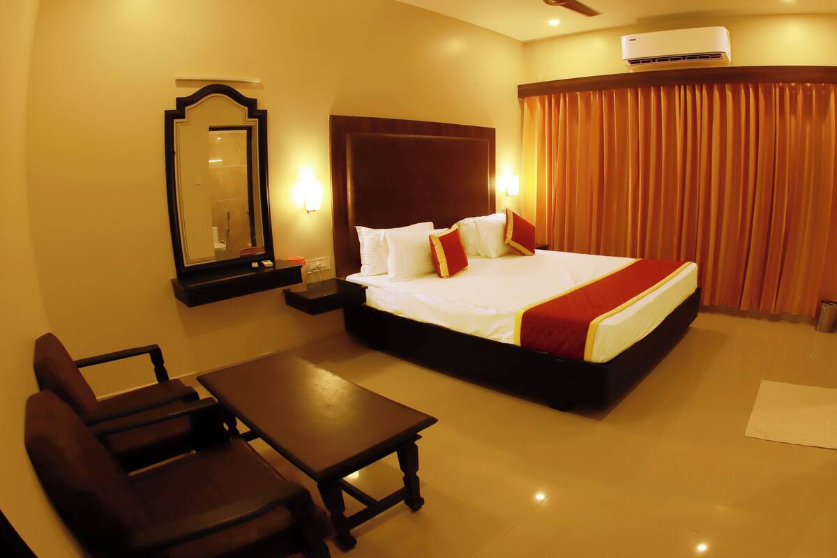 A hotel room with a bed, bedside table, chair, and a mirror.